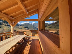 Eine Holzdar Terrasse mit Tisch und Bänken, mit Blick auf eine gebirgige Landschaft.
