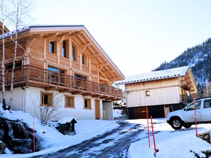 A wooden chalet with a balcony, a garage, and a snow-covered driveway.