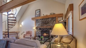 Een gezellige woonkamer met een stenen openhaard, een wenteltrap en een comfortabele zithoek.
