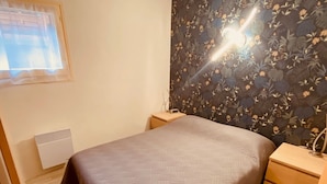Un dormitorio con cama, mesita de noche, calentador de pared y ventana con persianas.