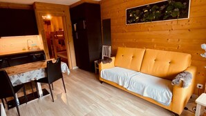 Una habitación acogedora con piso de madera, un sofá, una mesa de comedor con sillas y una zona de cocina.