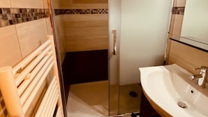 Un baño con cabina de ducha de vidrio, un lavamanos blanco y un perchero para toallas.