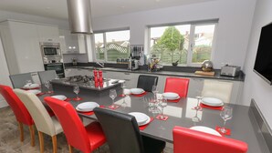 Een moderne keuken met een centraal eiland, rode en zwarte stoelen en een eettafel gedekt voor zes personen.