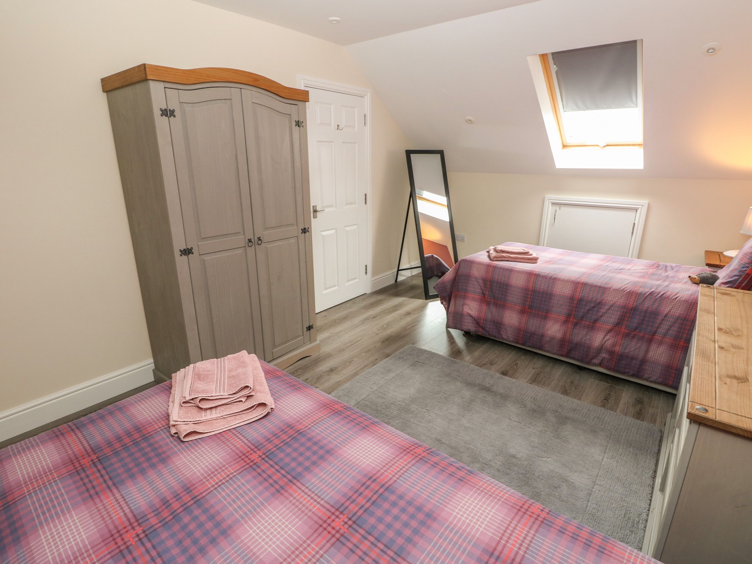 A bedroom with two beds, a wardrobe, a mirror, and a window.