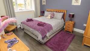 Een slaapkamer met een bed, een houten nachtkastje, een stoel, een tafel en een raam met gordijnen.