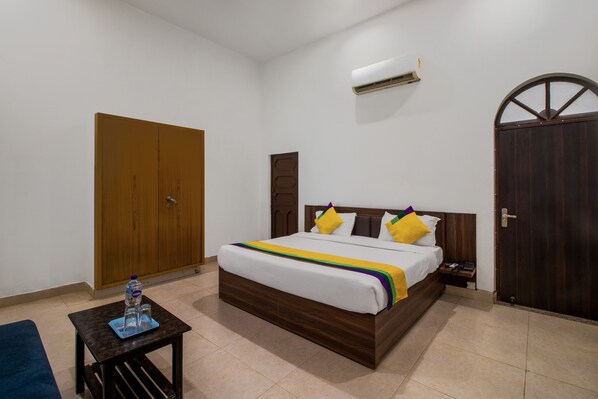 A bedroom with a wooden bed, a small table with a bottle, and a wardrobe. - Itsy Hotels Om Pushp Residency (Mathura)