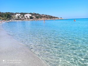 A beach with clear water, a few people, and buildings in the background.
