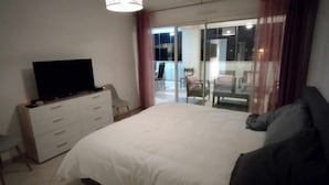 Een slaapkamer met een bed, een dressoir, een televisietoestel en een balkon met stoelen.
