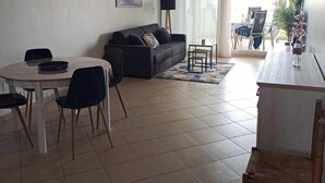 Een moderne woonkamer met een bank, een eettafel, stoelen en een kleine salontafel. Een klok en een ingelijst kunstwerk hangen aan de muur.