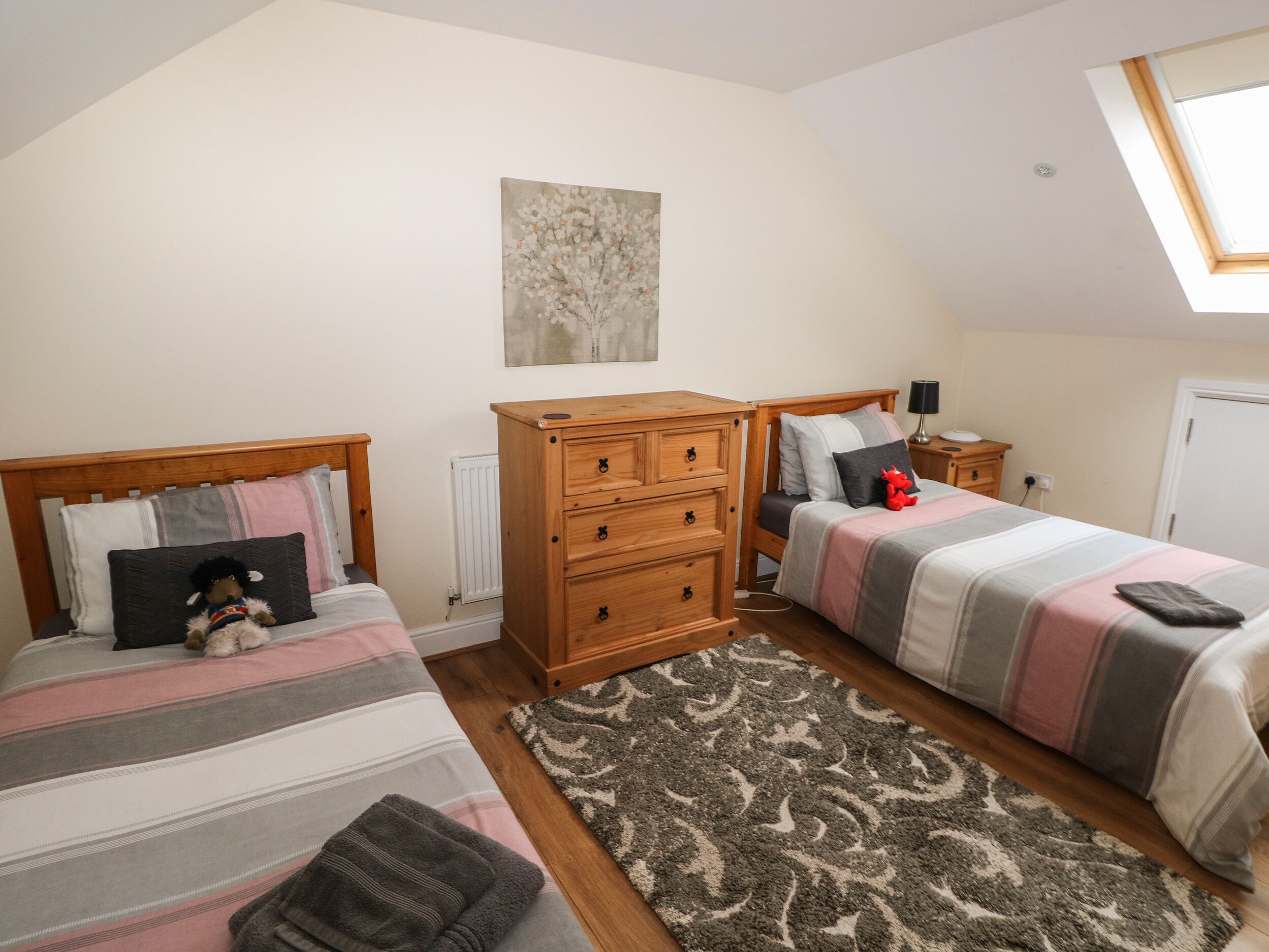 A bedroom with two beds, a wooden dresser, a nightstand, and a skylight.