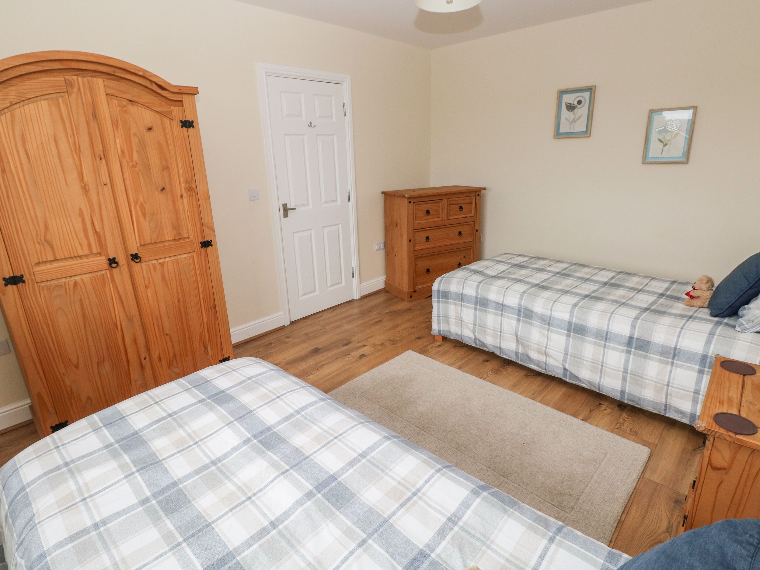 A bedroom with two beds, a wooden wardrobe, a dresser, and a door.