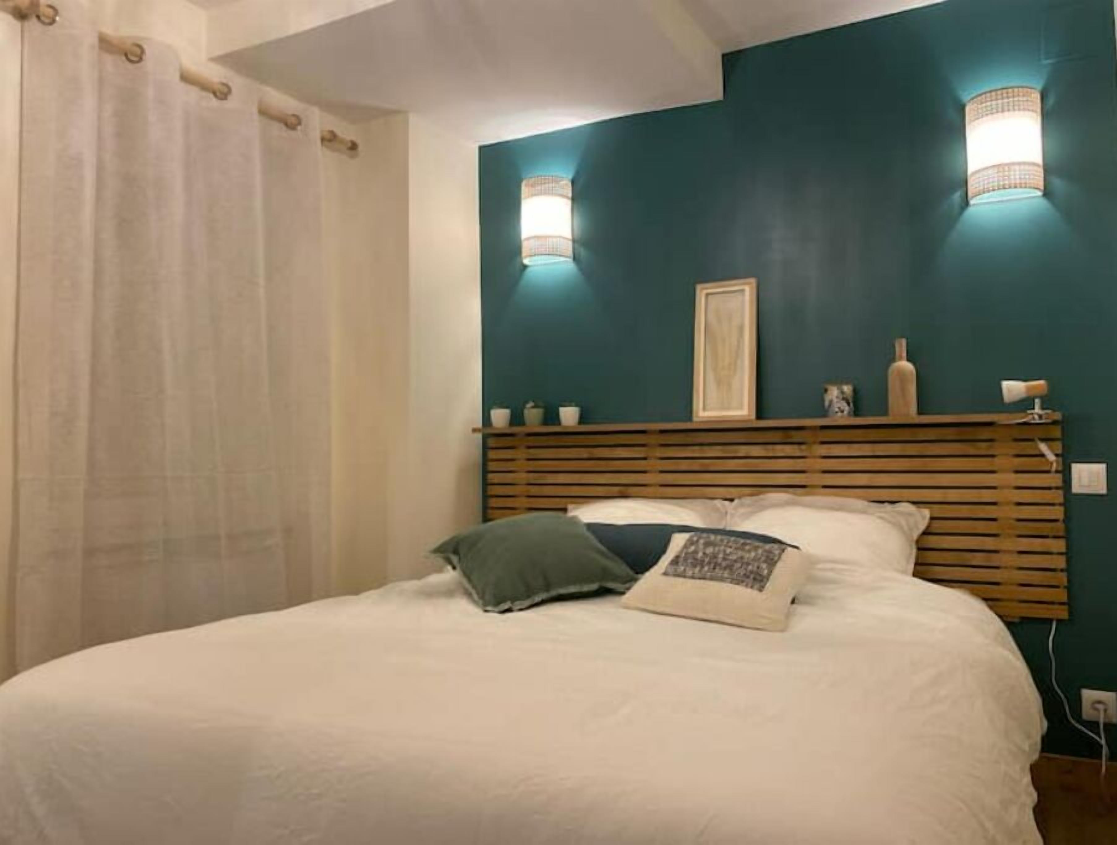 Een slaapkamer met een bed, een houten hoofdbord, twee wandlampen en een raam met gordijn.