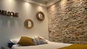 Een slaapkamer met een bed, een 'WELCOME' bord, een spiegel en een structuurwand van steen.