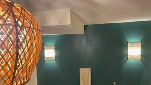 Een kamer met een houten spijlenbank, twee wandlampen en een hangende, oranje rasterlamp.