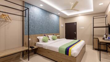 A modern hotel room with a wooden bed, a desk with a kettle, a wardrobe, and a ceiling fan.