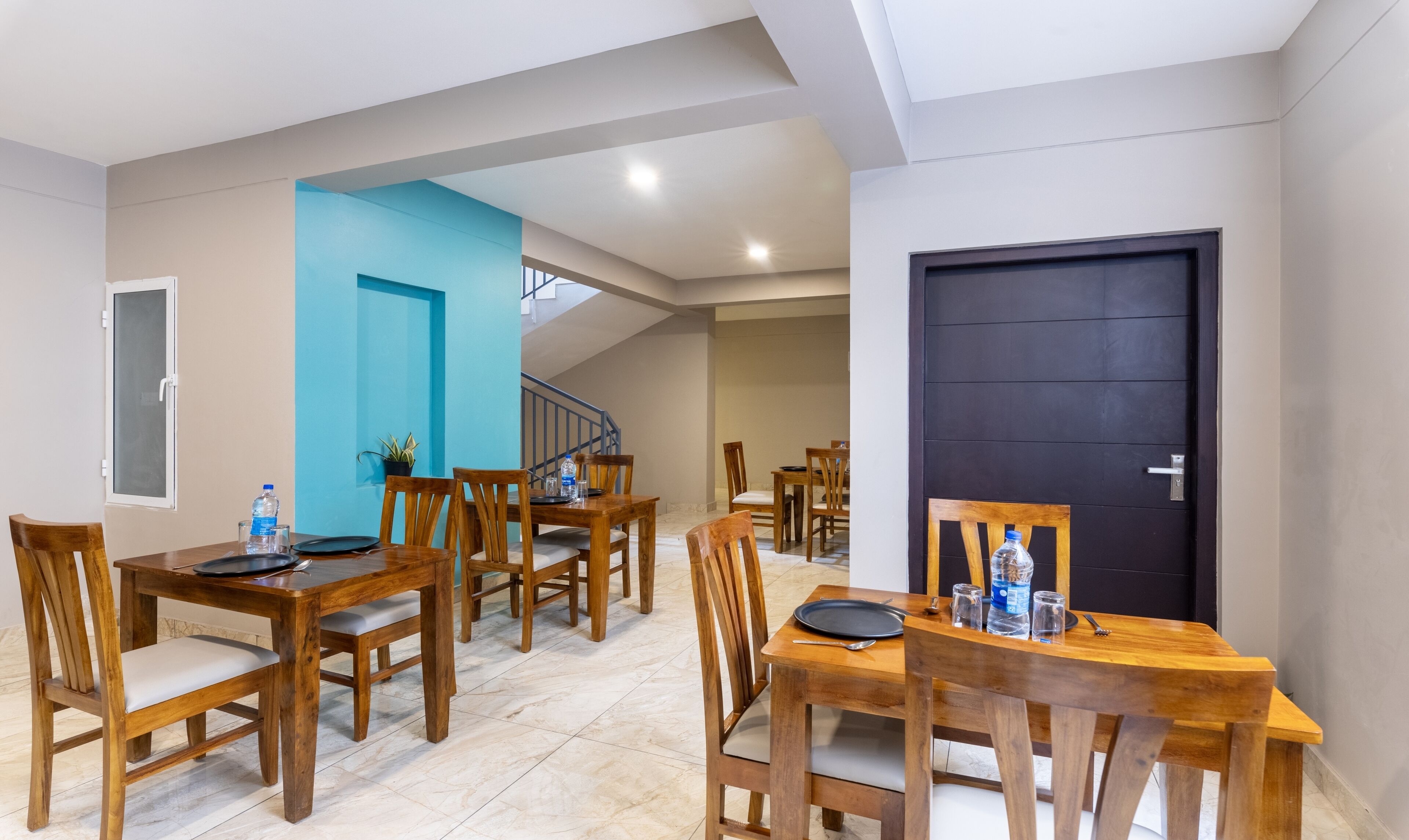 A dining area with wooden tables and chairs, a blue accent wall, and a black door.