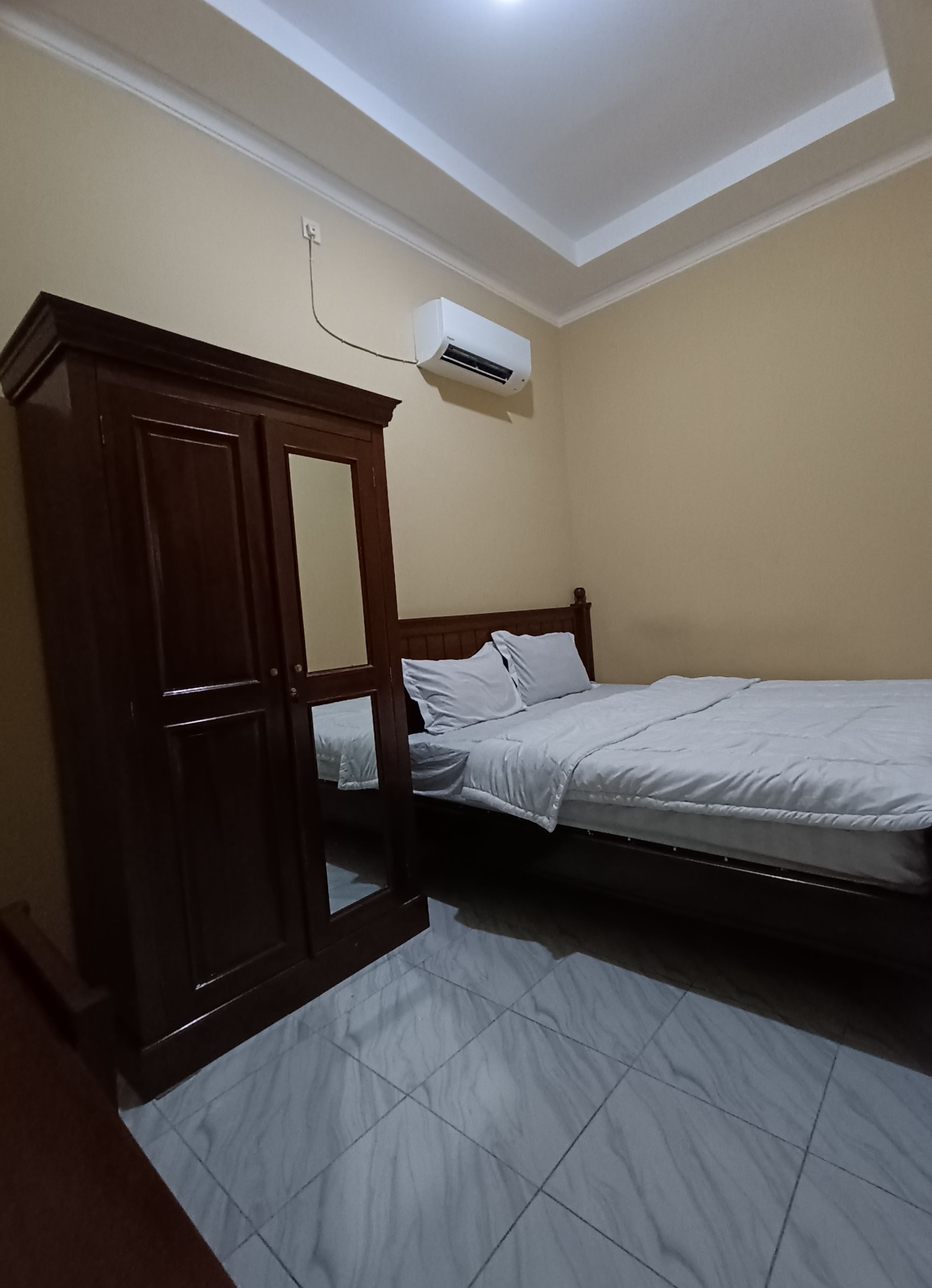 A bedroom with a bed, a wardrobe, and an air conditioning unit.