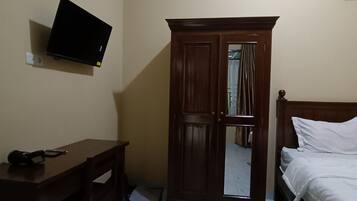 Ett rum med en säng, ett skrivbord, en garderob och en TV som är monterad på väggen.