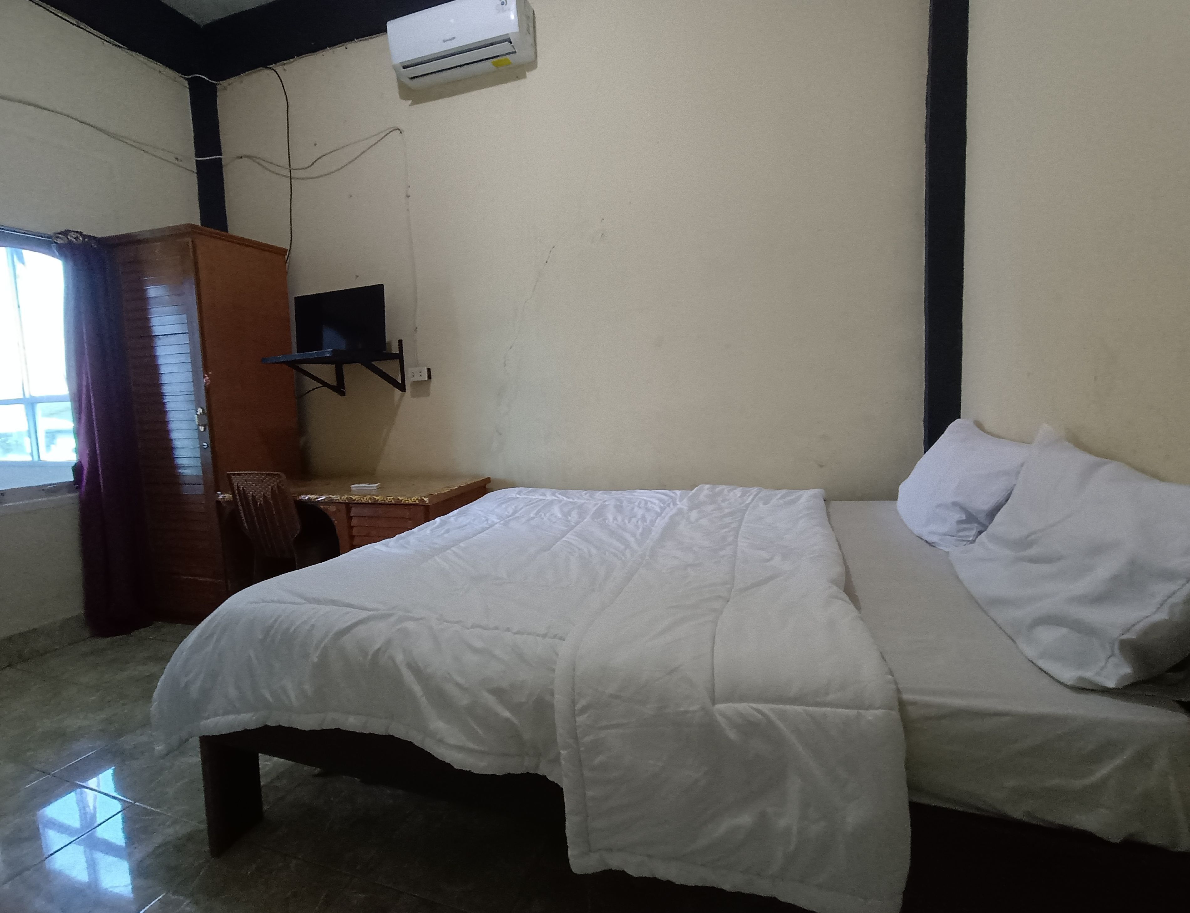 Una habitación con cama, un armario de madera, un televisor y una ventana con cortinas.