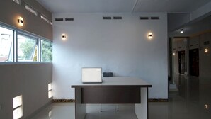 A modern, minimalist office space with a desk, a laptop, and a chair. There are windows providing natural light and a view of the outdoors. - Hotel O Ananda Homestay Syariah (Pekanbaru)