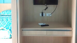 A small, enclosed room with a flat-screen TV mounted on the wall, a desk with a remote control, and a power outlet. - Hotel O Ananda Homestay Syariah (Pekanbaru)