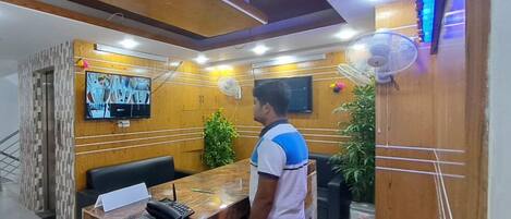 A reception area with a wooden reception desk, a television mounted on the wall, and a seating area with black chairs.