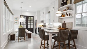 A modern kitchen with white cabinets, a central island, and striped chairs. - 5BR Victorian Carriage House | Near Forsyth Park (Savannah)