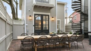 A patio with a wooden table and wicker chairs, a black door, and a spiral staircase. - 5BR Victorian Carriage House | Near Forsyth Park (Savannah)