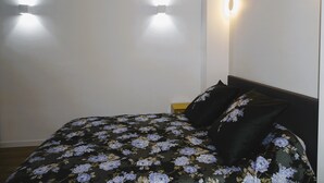 A bed with a floral bedspread and two pillows, a nightstand, and wall-mounted lights. - Augustins Fountain Studio AIX Centre Historique à 3 Minutes de Cours Mirabeau (Aix-en-Provence)