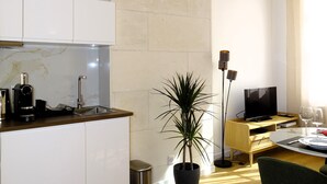 A modern kitchen with white cabinets, a marble backsplash, and a wooden ceiling. There's a dining area with a table, chairs, and a potted plant. - Augustins Fountain Studio AIX Centre Historique à 3 Minutes de Cours Mirabeau (Aix-en-Provence)
