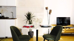A modern living room with a round dining table, two green upholstered chairs, a potted plant, and a television on a wooden stand. - Augustins Fountain Studio AIX Centre Historique à 3 Minutes de Cours Mirabeau (Aix-en-Provence)