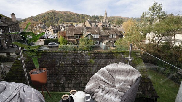 Ein gemütlicher Sitzbereich im Freien mit Blick auf ein Dorf, Steinmauern und einen Kirchturm in der Ferne.