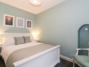 A neatly made bed with white bedding and a green throw, a bedside table with a lamp, and a chair with a green cushion. - Fell View (Ambleside)