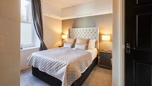 Un dormitorio ordenado con una cama grande, dos mesitas de noche y una puerta oscura.