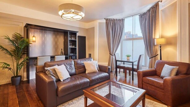 Una sala de estar moderna con sofás de cuero, una mesa de centro de vidrio y un comedor con mesa y sillas.