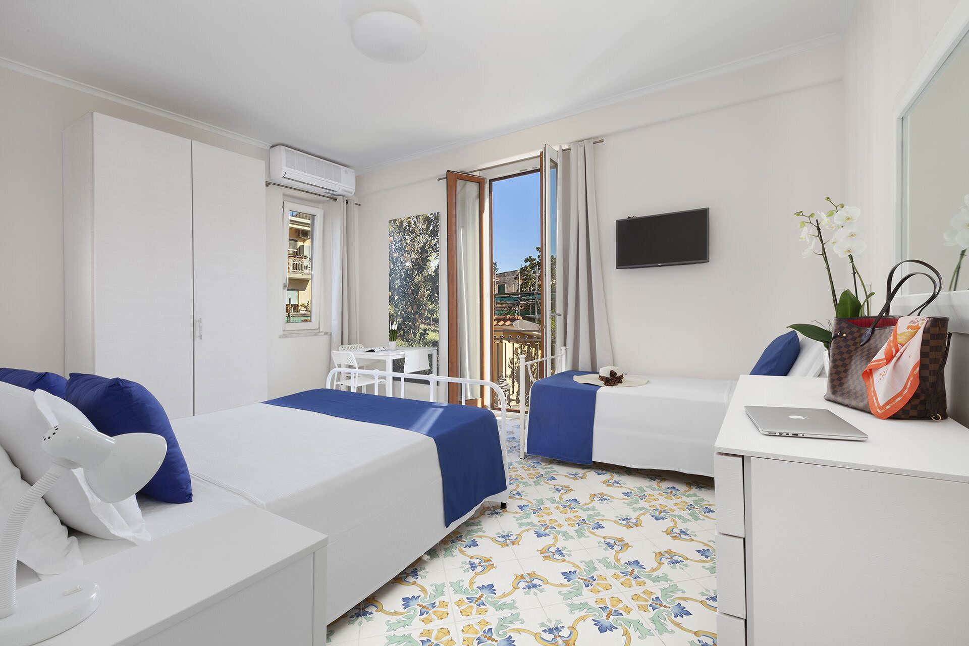Camera d'albergo con un letto, una scrivania con un portatile, un telefono, una televisione e un balcone con vista sull'esterno.
