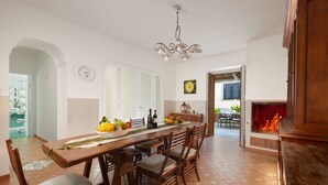 Zona pranzo con tavolo in legno, sedie, un lampadario e un camino.