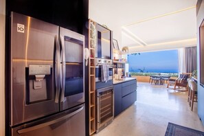 A modern kitchen with a stainless steel refrigerator, a built-in oven, and a coffee machine. There is a dining area with a view of the ocean. - Luxury 1BR + Flex | Heated Rooftop Pool | Soho PV (Puerto Vallarta)