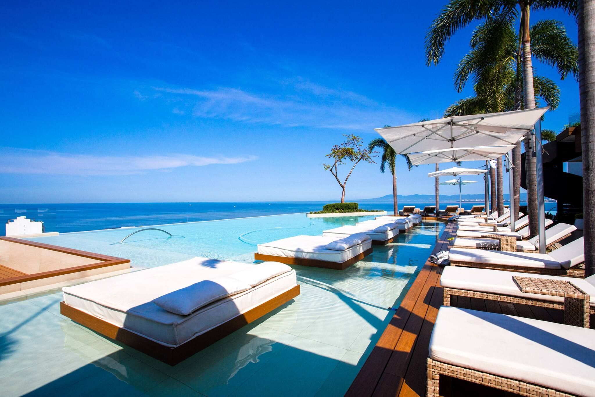 Une piscine à débordement avec des chaises longues et des parasols, offrant une vue imprenable sur une mer d’un bleu cristallin.