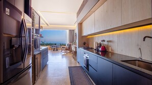 A modern kitchen with a view of the ocean, featuring stainless steel appliances, a red blender, and a large island with seating.