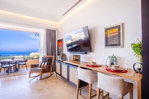 A modern hotel room with a balcony, a flat-screen TV, a dining area, and a bar.