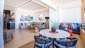 A modern living room with a round table, sofas, and a kitchen area visible through an open door.
