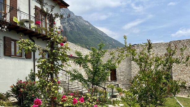 A stone building with a balcony, surrounded by lush greenery and pink flowers. - Villa del Lis (Gargnano)
