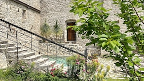 A stone building with a staircase leading to a pool area surrounded by lush greenery and flowers. - Villa del Lis (Gargnano)