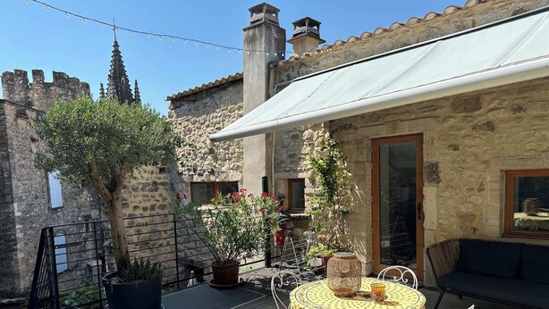 A courtyard with a round table, chairs, a sofa, and potted plants. - Les Deux Tours (Aiguèze)