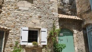 A stone building with a green door, a window with shutters, and a hanging street lamp. - Les Deux Tours (Aiguèze)