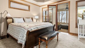 Une chambre à coucher avec un grand lit, un banc, un bureau et une vue sur l’extérieur, visible à travers une porte.