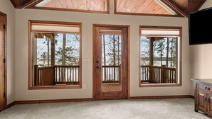 Une pièce avec un plafond haut, des poutres en bois et de grandes fenêtres dotées de garde-corps en bois.