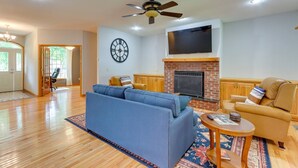 A spacious living room with a blue sofa, a tan armchair, a fireplace, and a ceiling fan.