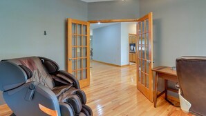 A spacious room with a massage chair, a dining table, and a kitchen area visible through an open door.